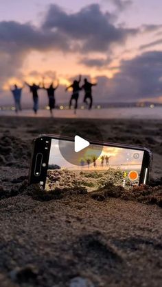 a cell phone sitting on top of a sandy beach next to the ocean at sunset