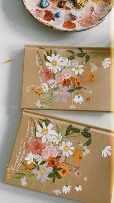 two cards with flowers painted on them next to a bowl of candy