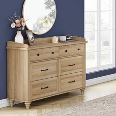 a dresser with a mirror and vase on it in front of a blue painted wall