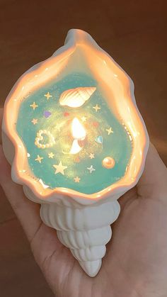 a hand holding a lit up candle in the shape of a shell with stars and planets on it