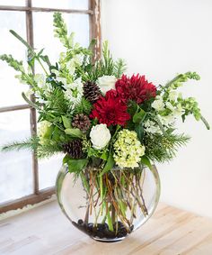 a vase filled with flowers and greenery on top of a wooden table next to a window