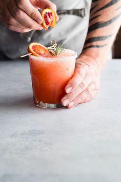 a person holding a grapefruit and garnish on top of a drink