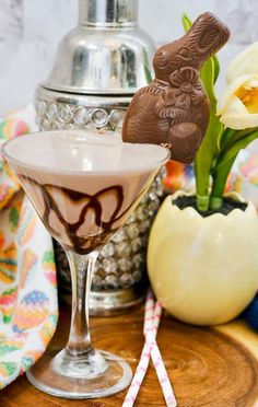 a glass filled with liquid and chocolate on top of a wooden table next to a vase