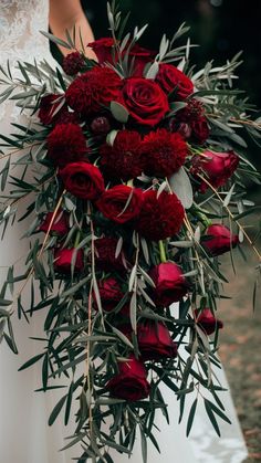 a bride holding a large bouquet of red roses and greenery in her wedding dress