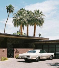 an old white car parked in front of a house with palm trees on the roof