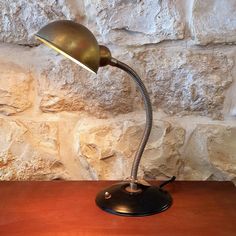 a desk lamp sitting on top of a wooden table next to a stone wall with a brick wall behind it