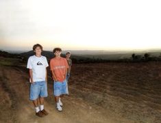 two young men standing next to each other on a dirt road in the middle of a field