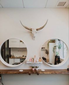 two round mirrors are mounted on the wall above a shelf with candles and other items