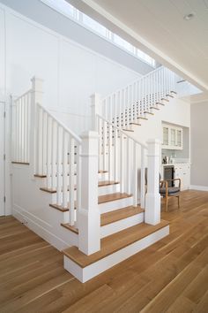 a white staircase with wooden floors and hard wood flooring in an open concept home