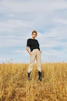 a woman standing in the middle of a field with her hands on her hips and looking at the camera