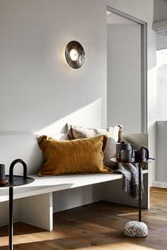 a white bench with pillows on it and a light fixture hanging from the wall above