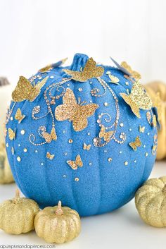 a blue pumpkin with gold butterflies on it and two golden pumpkins next to it