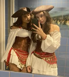 two women in costumes taking a selfie in a bathroom mirror while wearing pirate garb