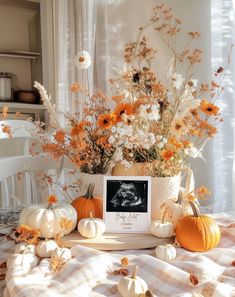 an arrangement of flowers and pumpkins on a table with a baby's photo