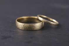 two gold wedding rings sitting on top of a black surface with one ring in the middle