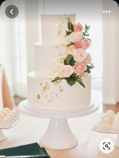 a white wedding cake with pink flowers on top and gold leaf decoration, sitting on a table