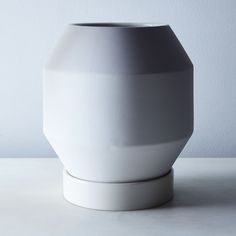 a white vase sitting on top of a table next to a gray and white wall