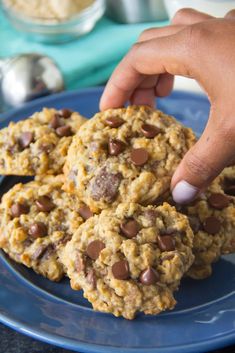 a person picking up chocolate chip cookies on a blue plate