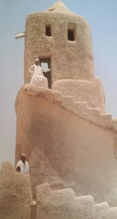 two men are standing in front of a stone structure with steps and a cross on top