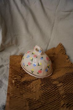 a small ceramic teapot sitting on top of a brown tablecloth covered bed sheet