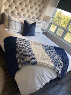 a bed with white and blue blankets on top of it next to a large window