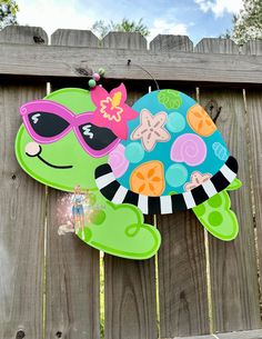 a paper cut out of a turtle with sunglasses on it's head is hanging from a wooden fence