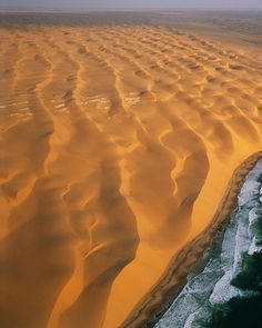 an aerial view of sand dunes in the desert, with waves coming up from them