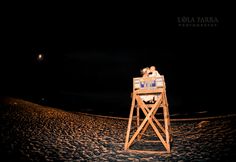 a lifeguard tower on the beach at night with its lights on and some people sitting in it