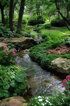 a stream running through a lush green forest filled with lots of trees and flowers next to rocks