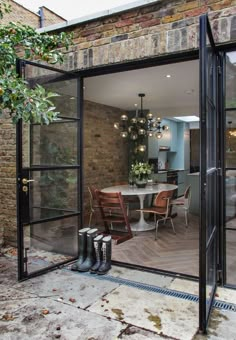 an open glass door leading into a dining room and kitchen area with brick walls, wood floors and flooring