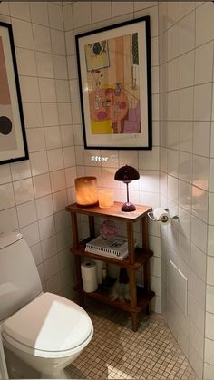 a white toilet sitting next to a wooden shelf in a bathroom under a painting on the wall