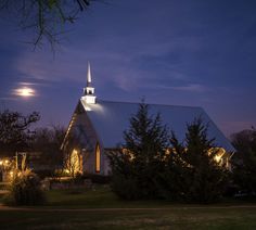 a church lit up at night with the moon in the sky above it and trees