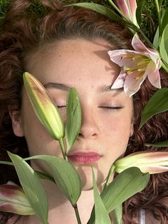 a woman with her eyes closed laying on the ground next to flowers and leaves in front of her face