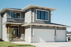 a two story house with gray siding and white garage doors on the front door is shown