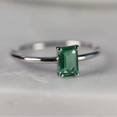 an emerald ring sitting on top of a white surface with a diamond in the middle