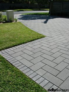 a brick walkway in the middle of a yard with green grass and trees behind it