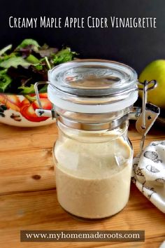 a glass jar filled with liquid sitting on top of a wooden table next to a bowl of salad