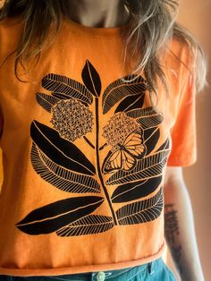 a woman wearing an orange t - shirt with black leaves and flowers on the front