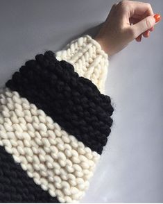 a woman's hand holding onto a black and white knitted sweater