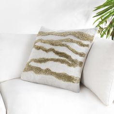 a close up of a pillow on a white couch with a plant in the background