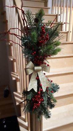 a christmas wreath on top of a banister with red berries and pine cones hanging from it