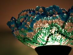 a green and blue glass bowl sitting on top of a wooden table next to a vase