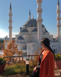 a woman sitting on a bench in front of a large white building with many spires