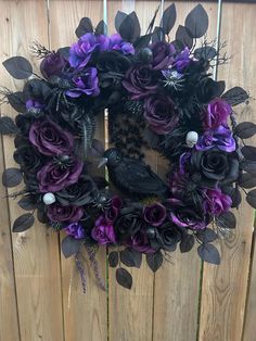 a wreath with purple and black flowers is hanging on a wooden fence next to a bird