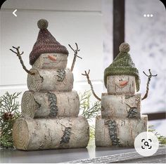 two snowmen made out of logs sitting on top of a table next to each other