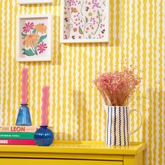 a yellow and white striped wall with vases, flowers and pictures on the wall