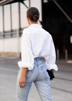 a woman in white shirt and jeans walking down the street with her hand on her hip