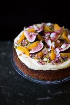 a cake topped with fruit and nuts on top of a glass platter filled with frosting