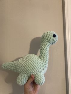 a hand holding a stuffed toy in the shape of a dinosaur