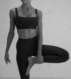 a woman standing on one leg with her hands in the air while wearing black sports bra top and leggings